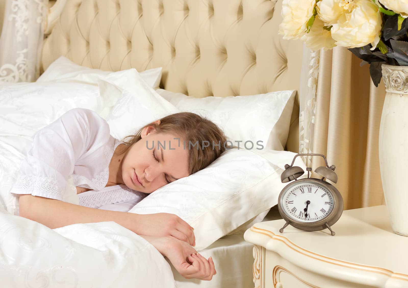 Beautiful sleeping woman resting in bed with alarm clock ready to wake her in the morning.