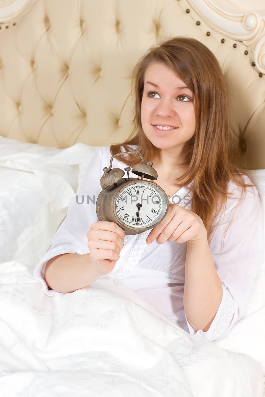 Young woman with alarmclock on the bed at the morning