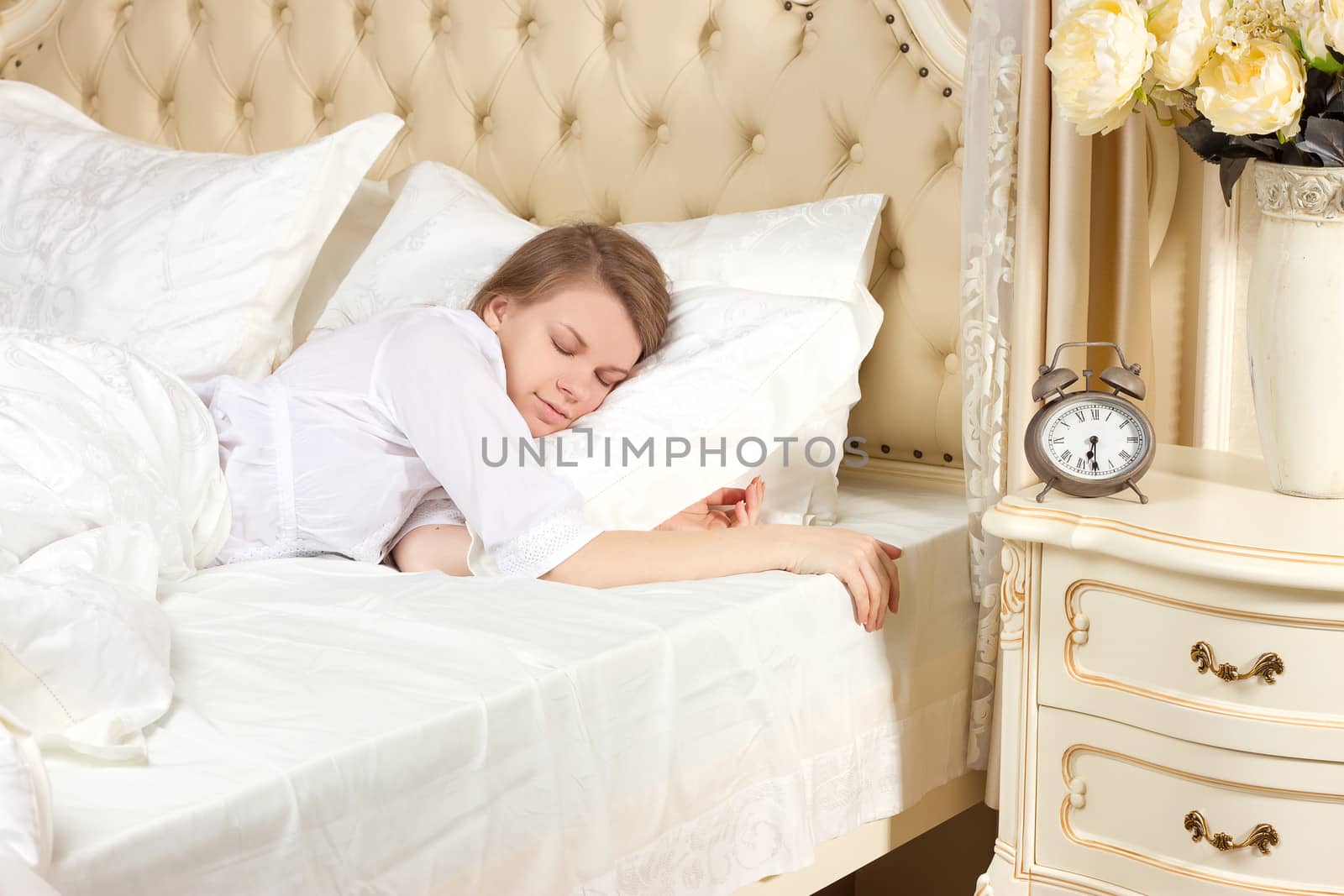 Beautiful sleeping woman resting in bed with alarm clock ready to wake her in the morning.