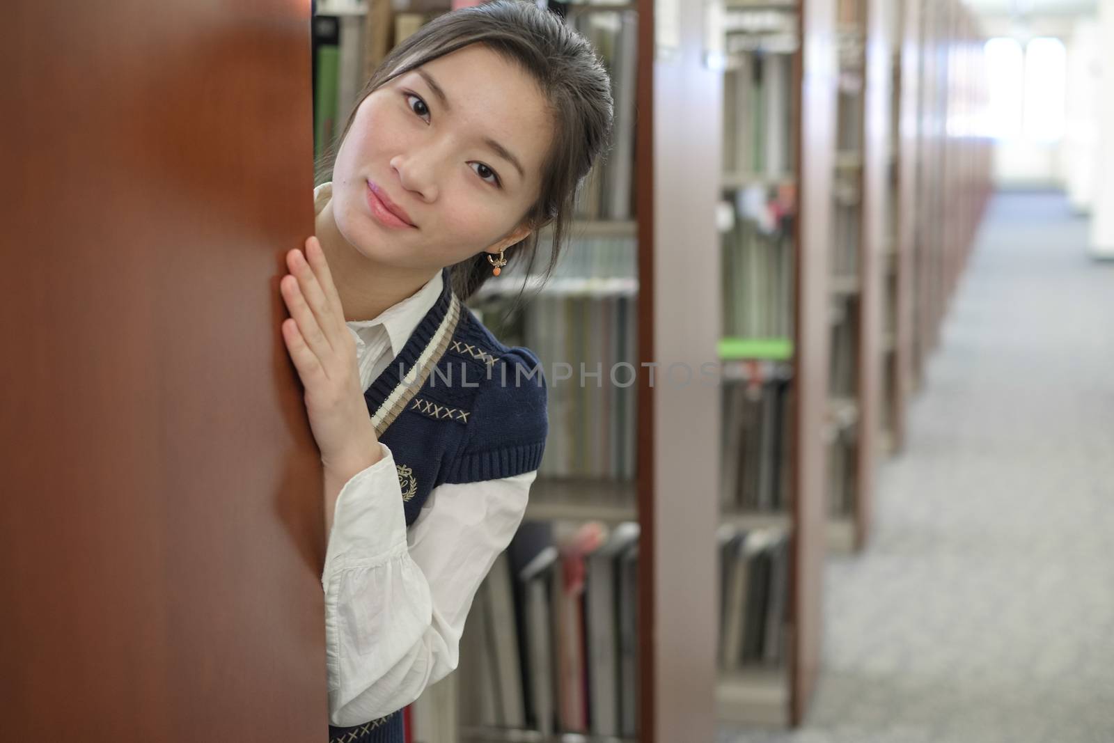 Girl hiding behind bookshelf by IVYPHOTOS