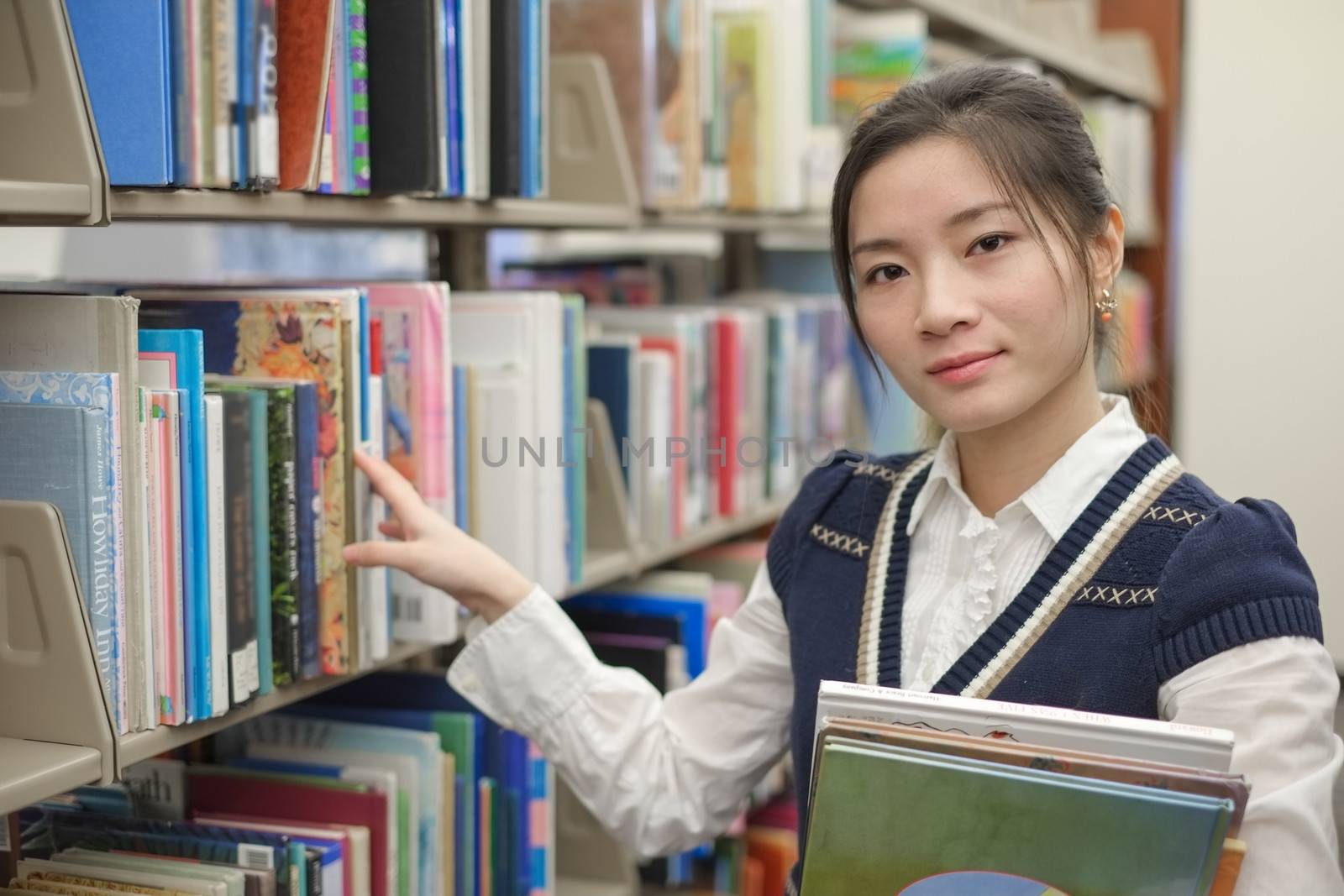 Intelligent young girl holding books and looking for books on a library shelf