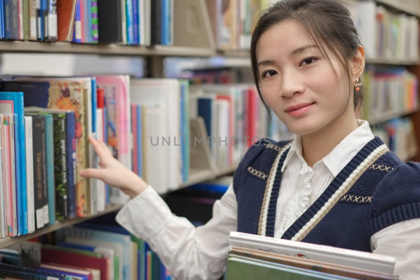 Intelligent young girl holding books and looking for books on a library shelf