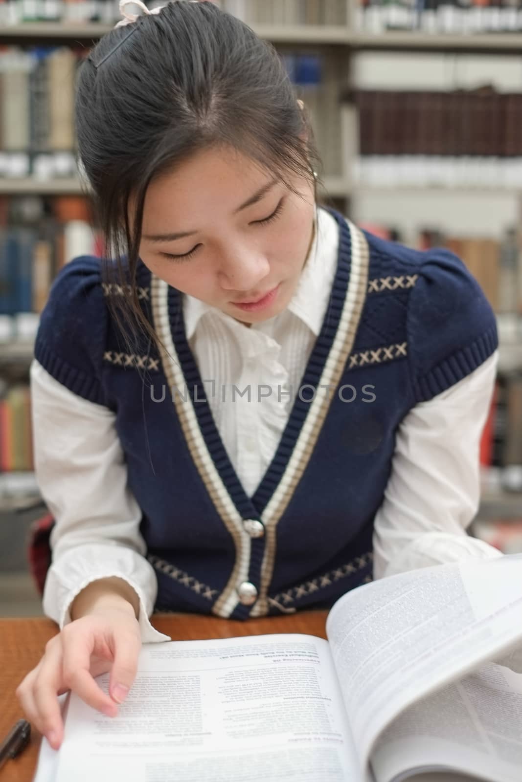 Portrait of young female student reading a textbook in front of library bookshelf