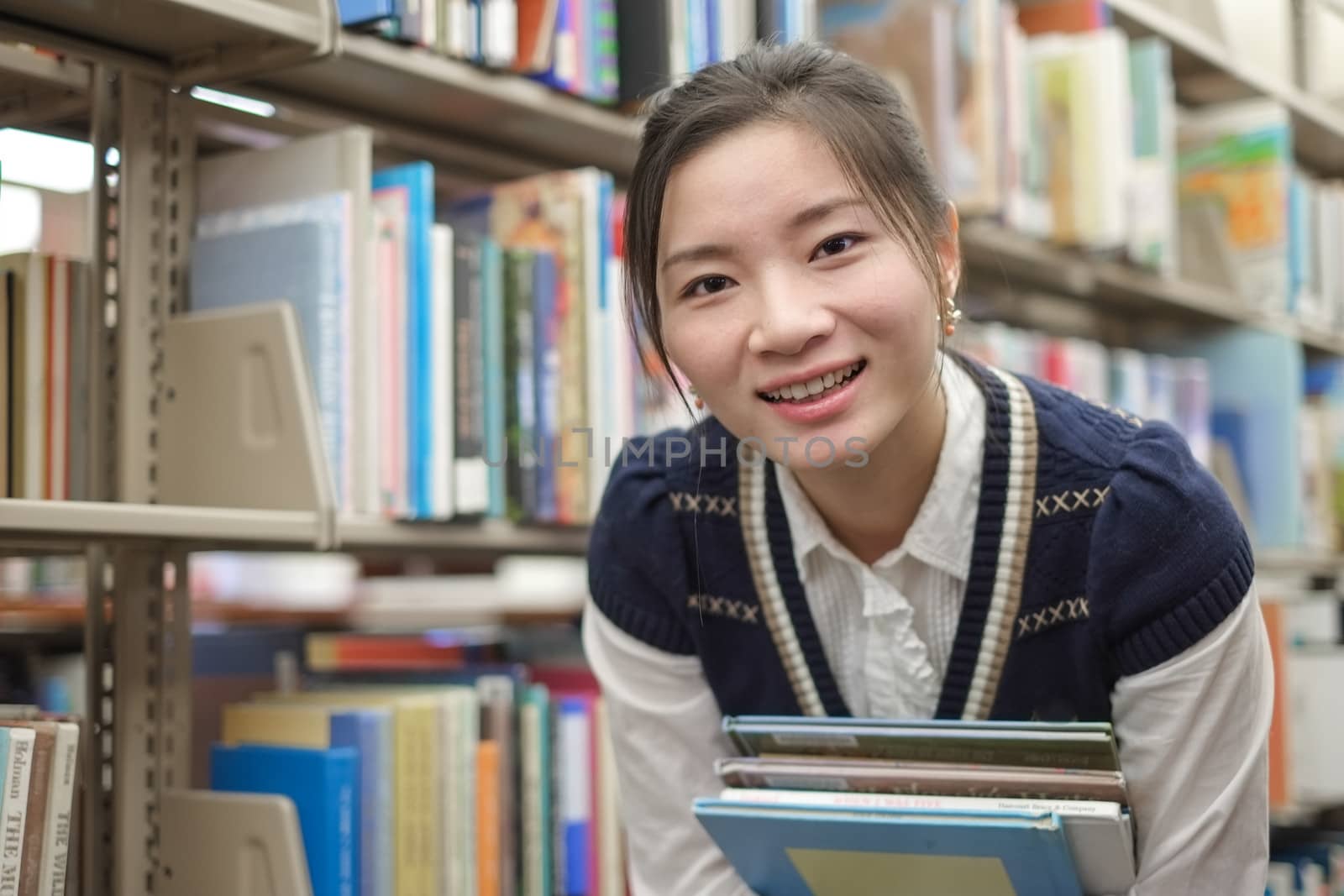 Young student holding books near bookshelf by IVYPHOTOS