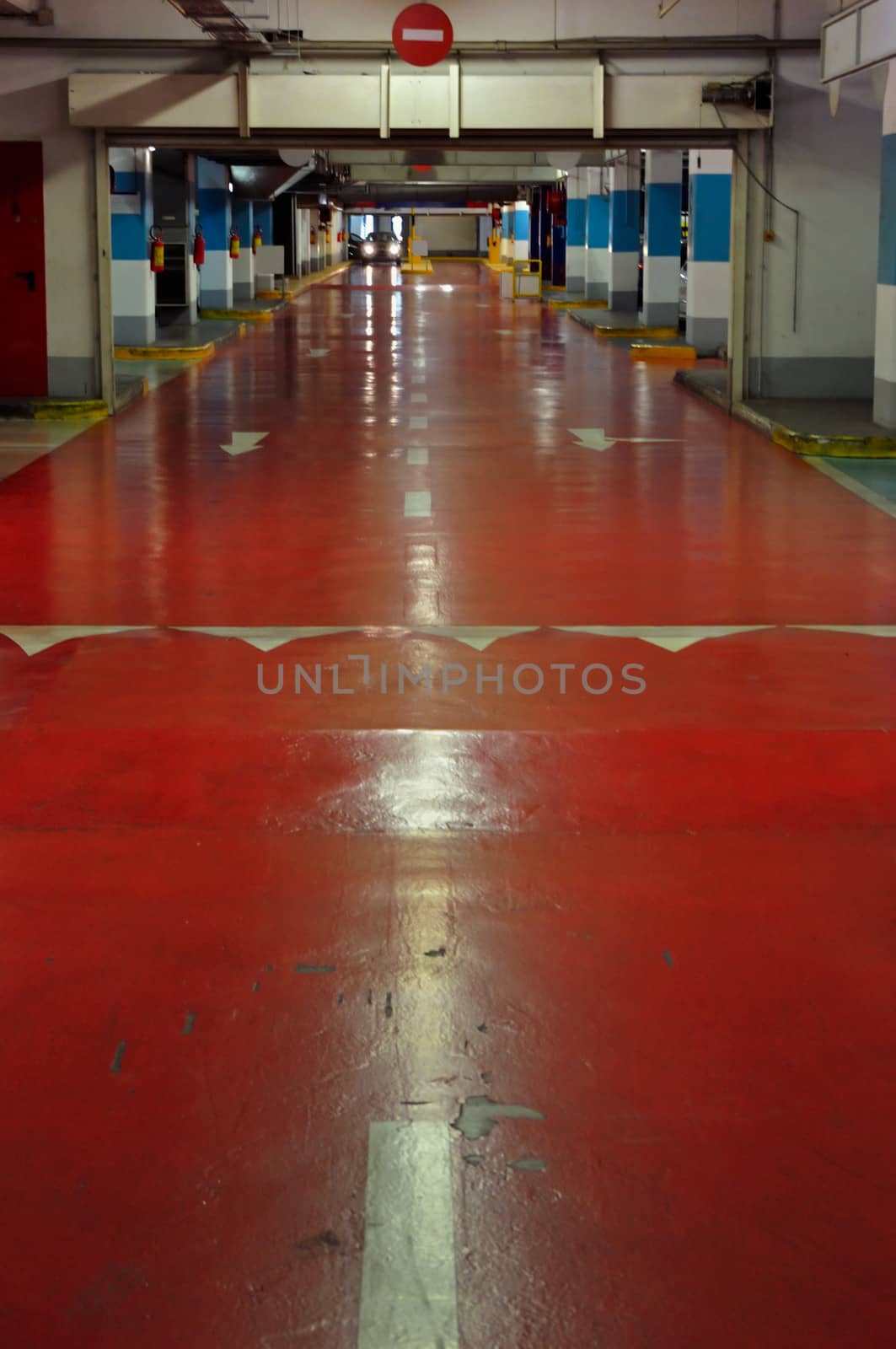 Underground multi-storey car park interior. Red driveway and approaching car.