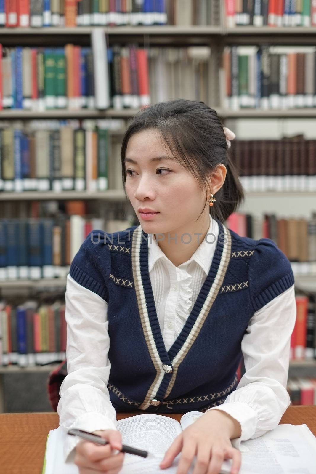 Portrait of young female student on sitting at a desk in front of a library shelf