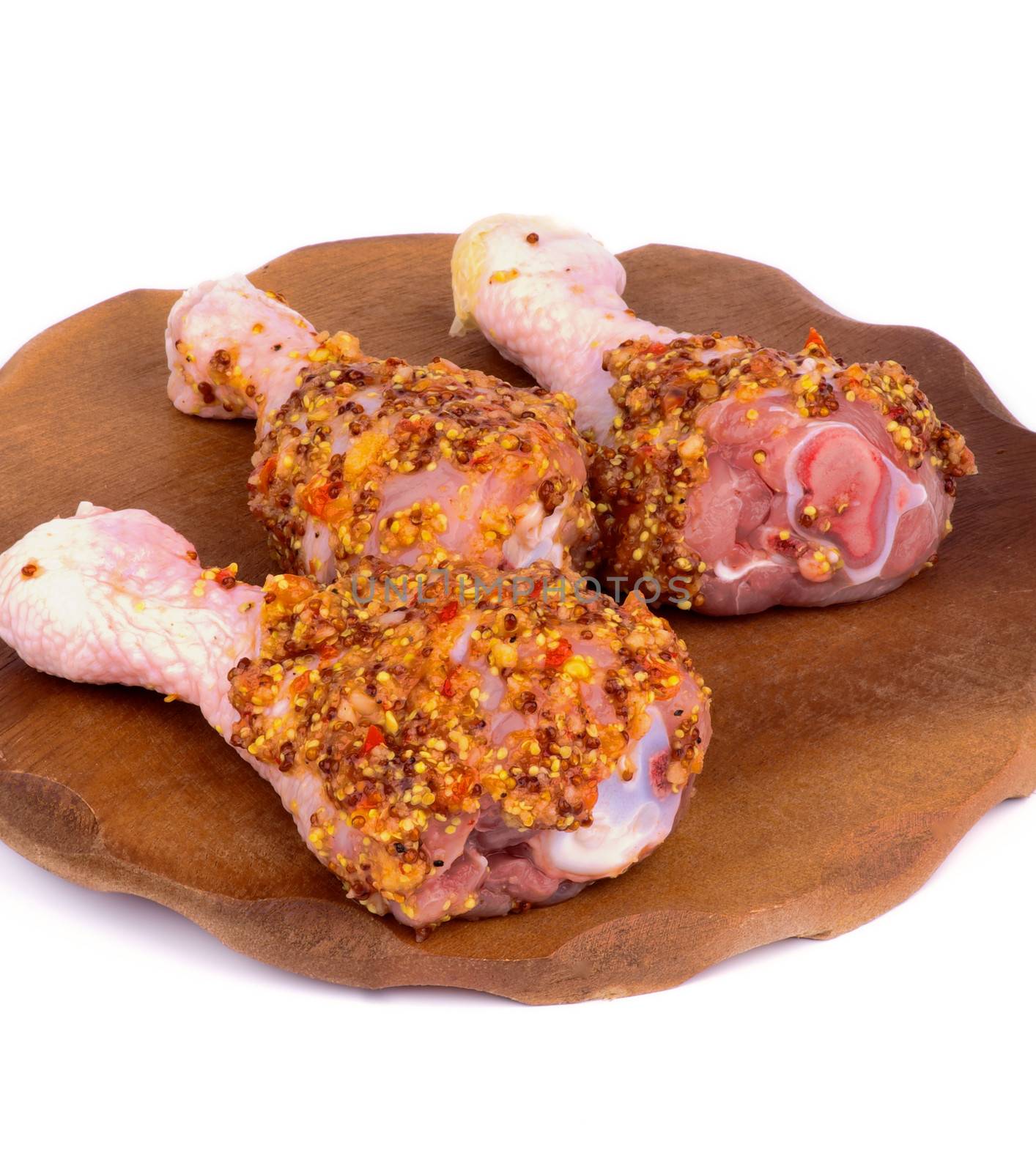Three Raw Chicken Drumsticks Marinated with Whole Grain Mustard closeup on Wooden Plate on white background 
