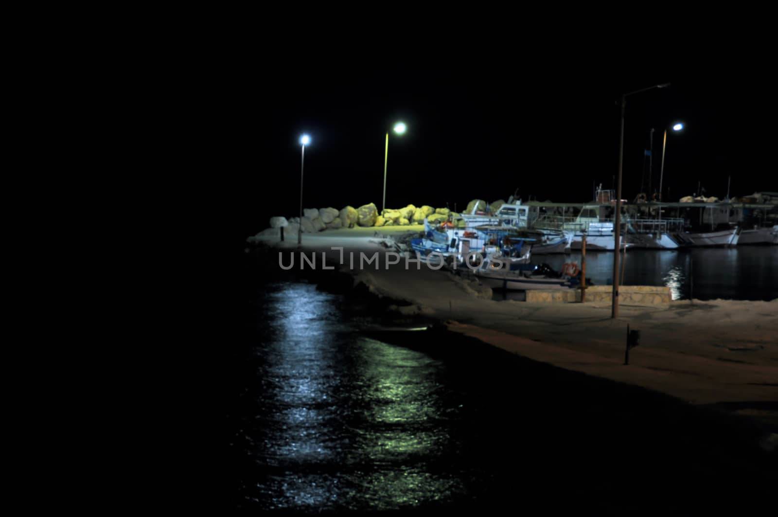 Empty pier and boats dark night. Street light reflections on black sea.