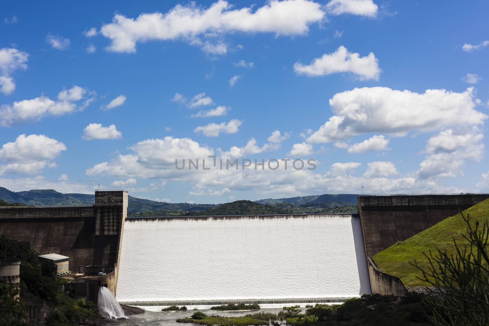 Dam filled to capacity with volumes of water flowing over the high wall on a summers day.