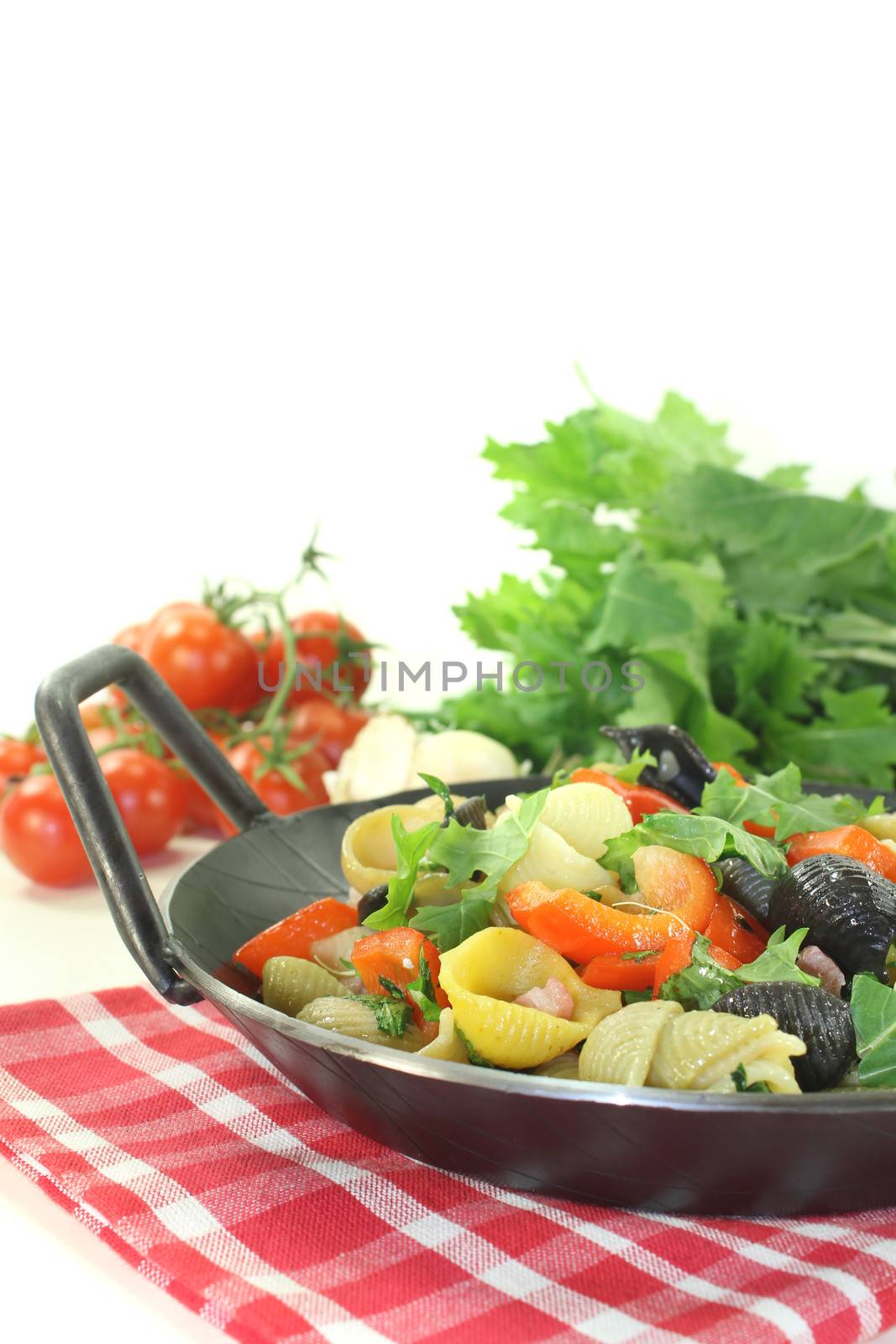 Pasta pan with bell pepper, turnip greens and ham strips on a light background