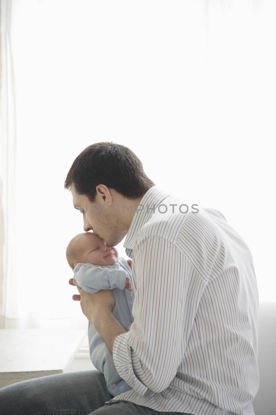 father kisses two week old newborn babies head by moodboard