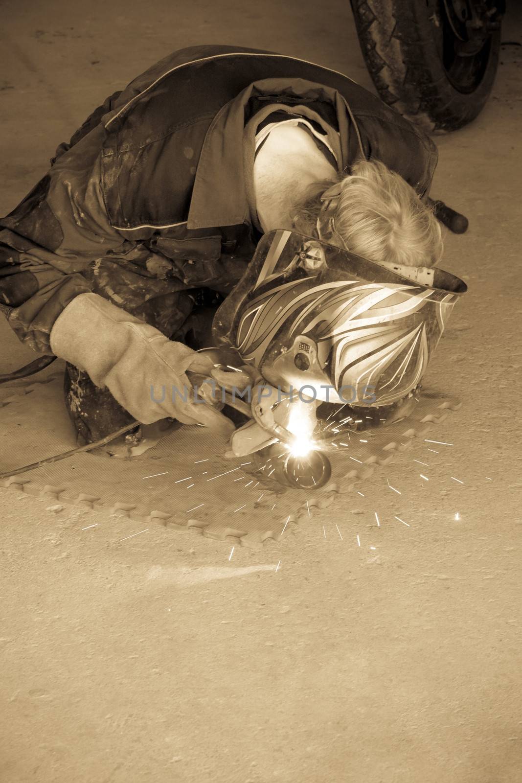 a mechanic welding the exhaust of a motorbike in a garage in sepia