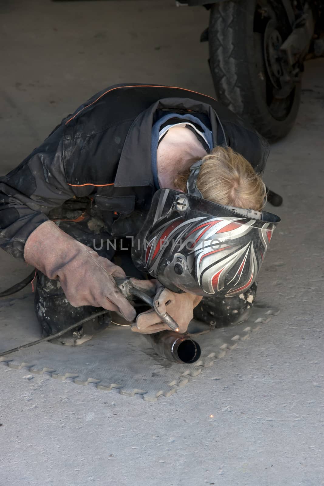 a mechanic welding the exhaust of a motorbike in a garage