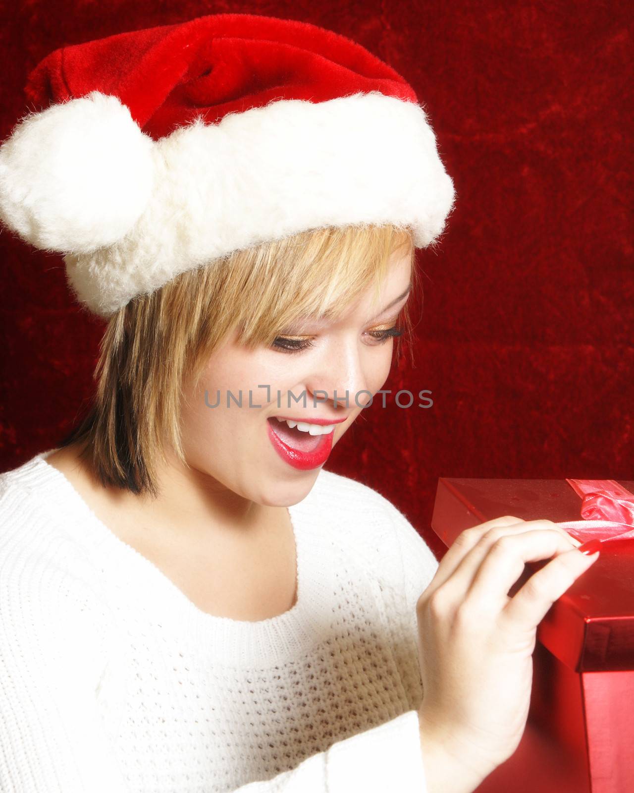 An attractive young woman opens a gift on Chrsitmas.