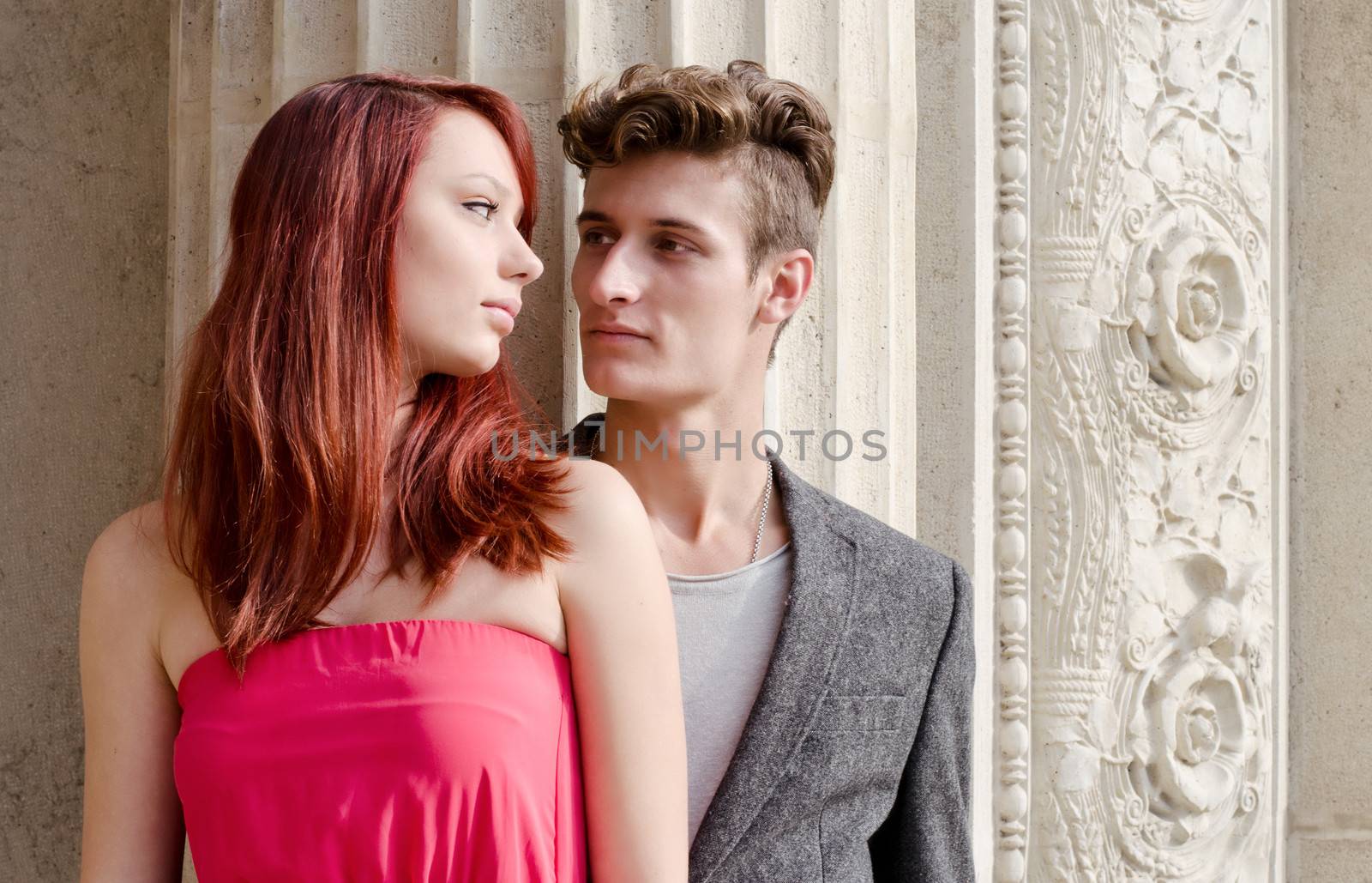 Elegant young couple standing in front of old stone column looking at each other