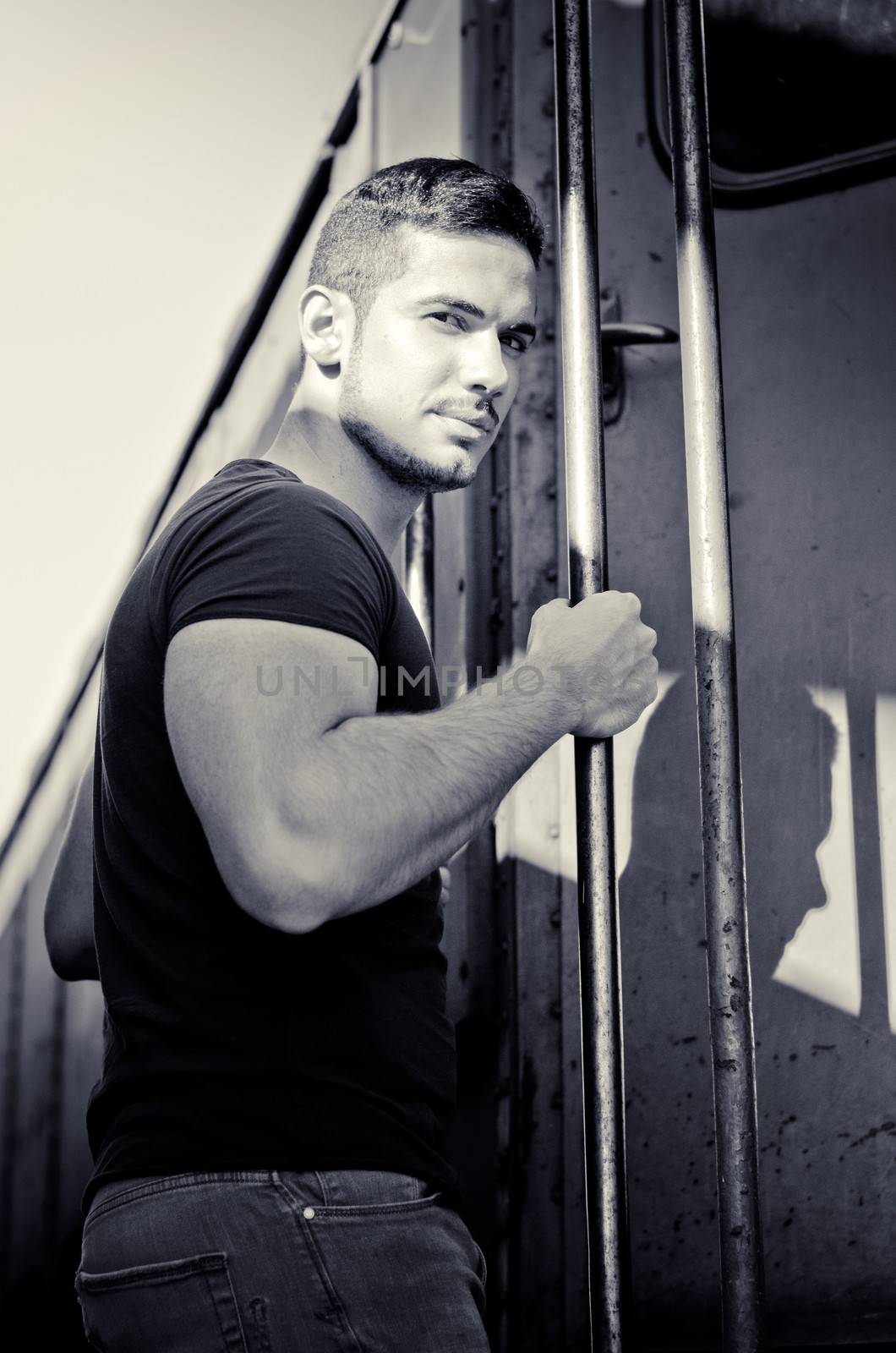Handsome young man hanging from train handle, looking at camera