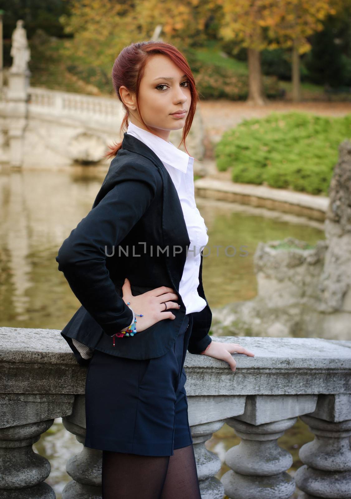 Elegant red-head girl outdoors against stone banister looking at camera
