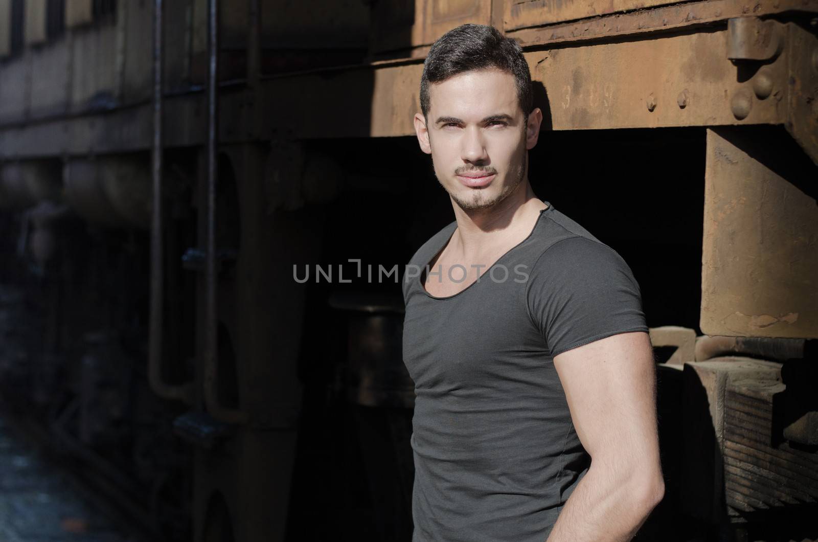 Attractive young man in dark t-shirt in front of old train looking at camera