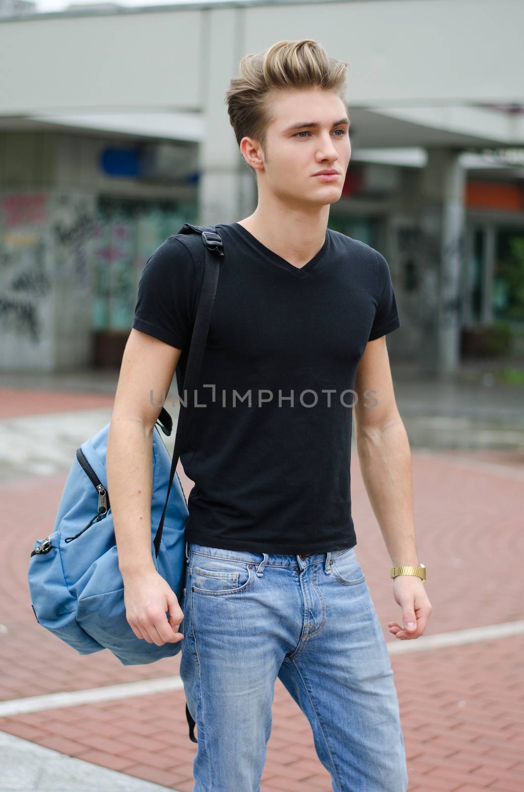 Attractive young man standing in city environment, with rucksack on one shoulder