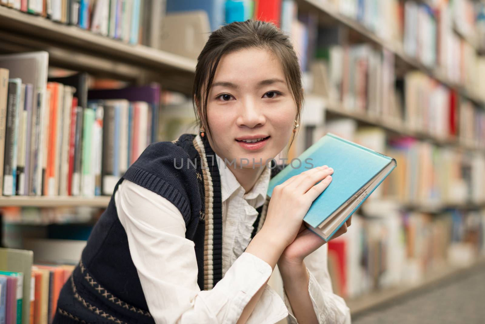 Happy young attractive woman holding a book while sitting in front of a bookshelf