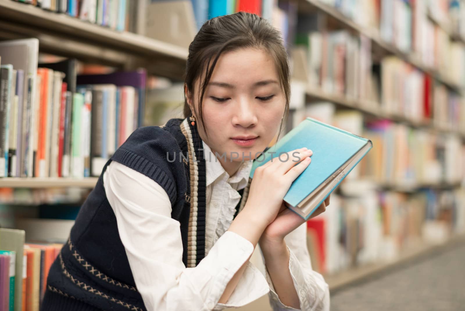 Upset young attractive woman holding a book while sitting in front of a bookshelf