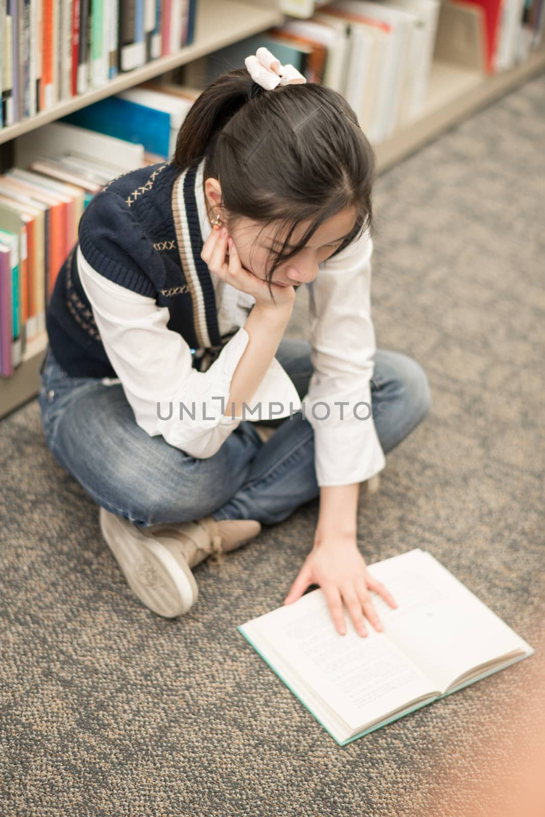 Young attractive woman reading a book while sitting on the floor in front of a bookshelf