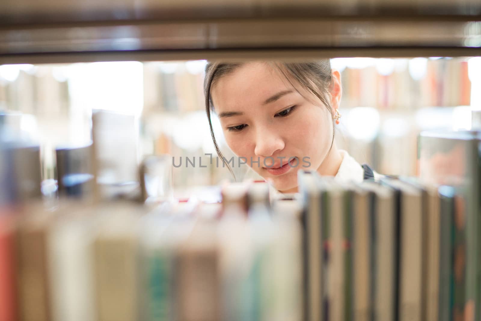 Attractive young woman looking for a book from a bookshelf in library