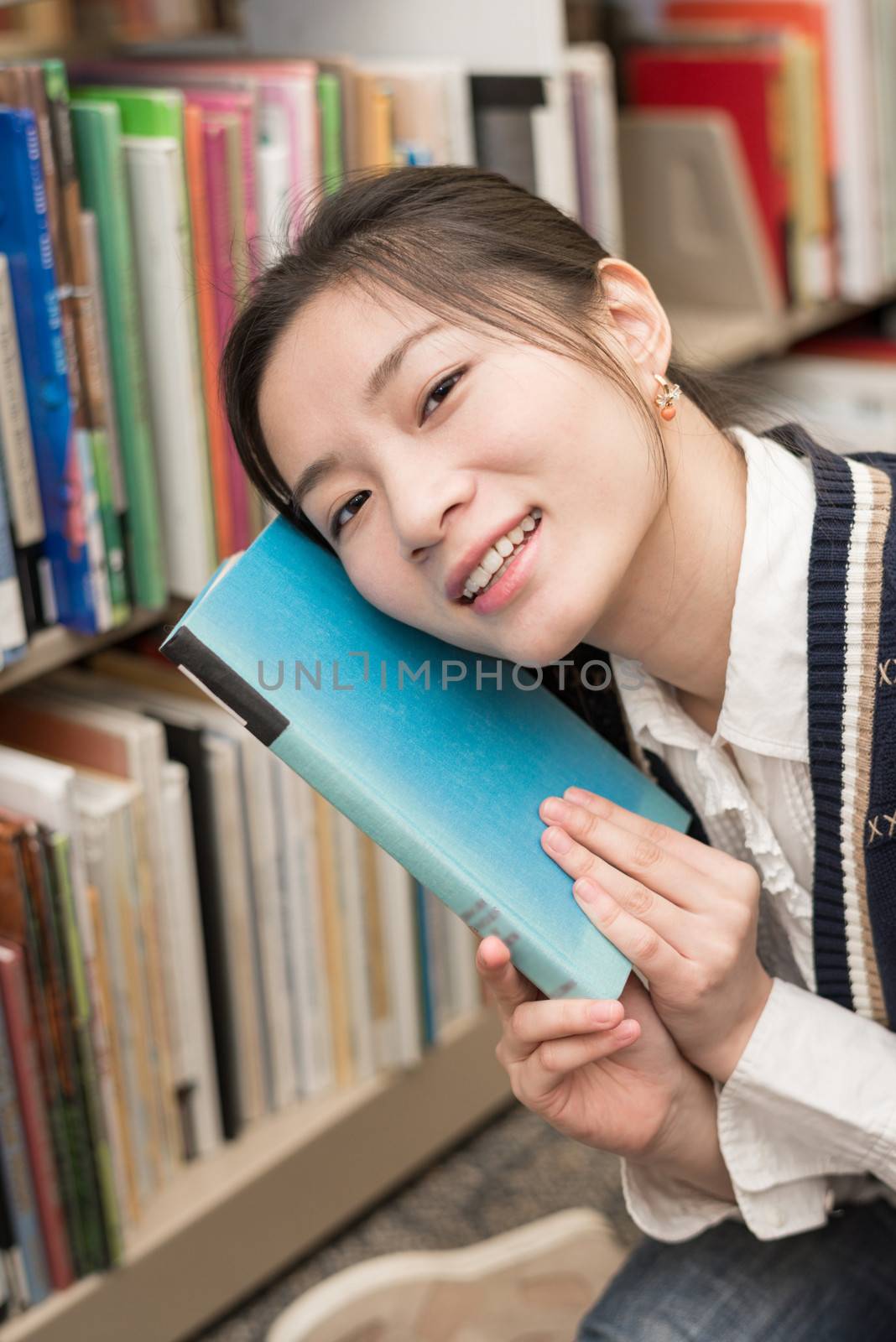 Portrait of young girl holding a blue book against her face next to a bookshelf