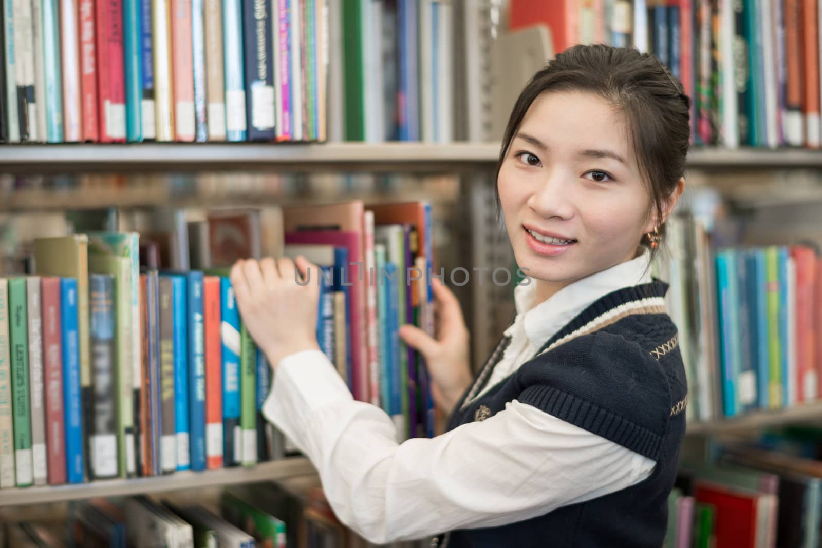 Portrait of young clever student standing in front of a bookshelf in library