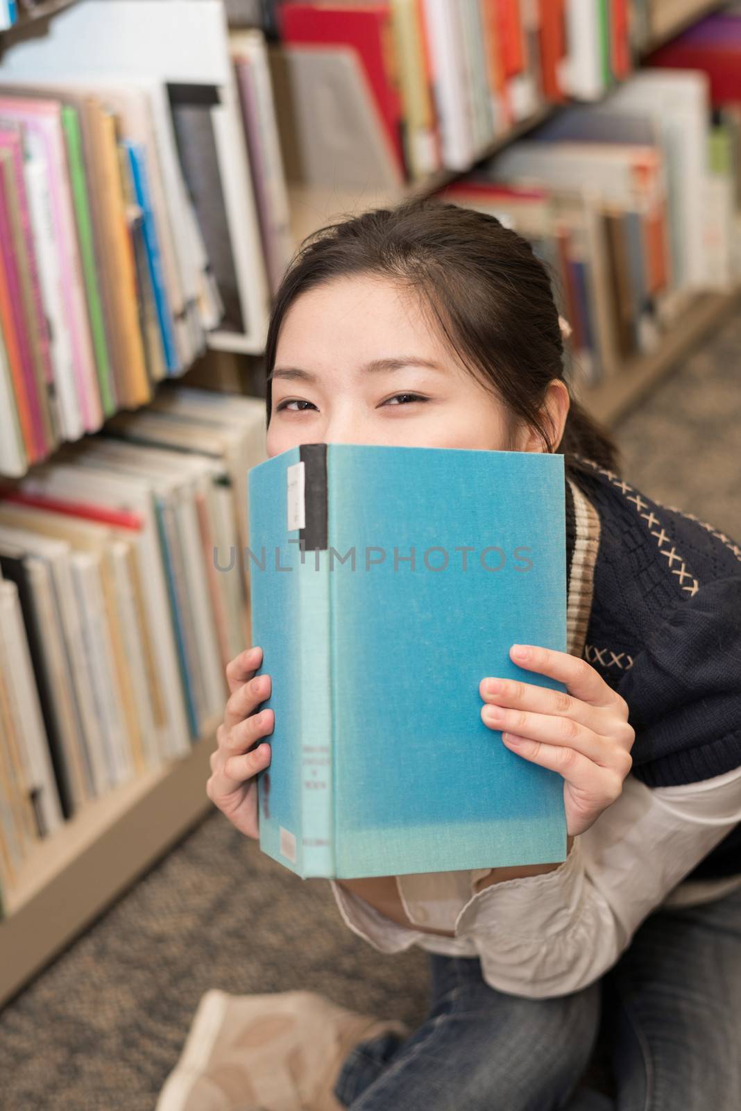 Playful student covering mouth with a blue hard cover book in library