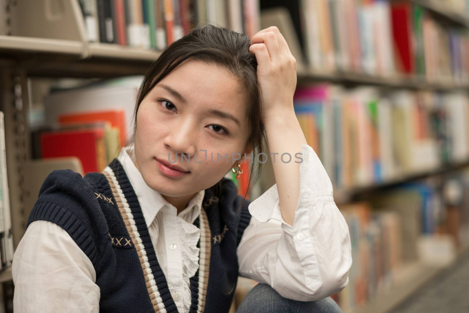 Portrait of stressed young girl next to a bookshelf supporting head with one arm