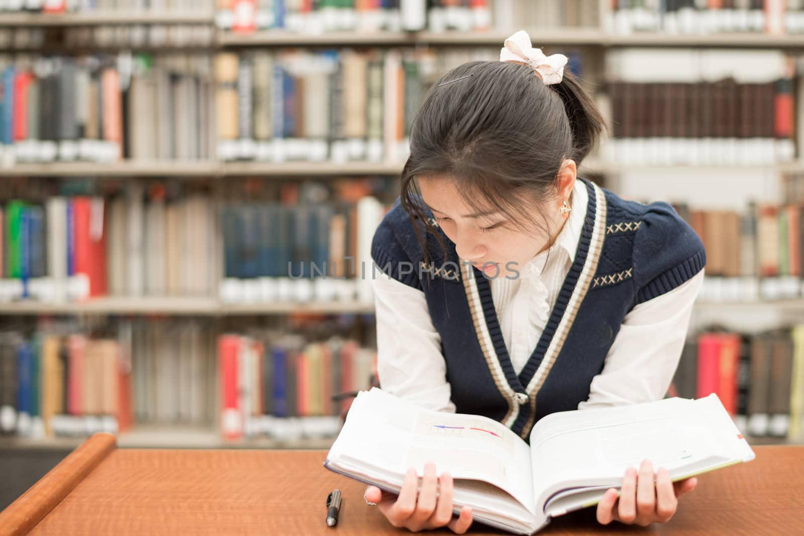Pretty female student sitting at a desk reading a testbook in the library