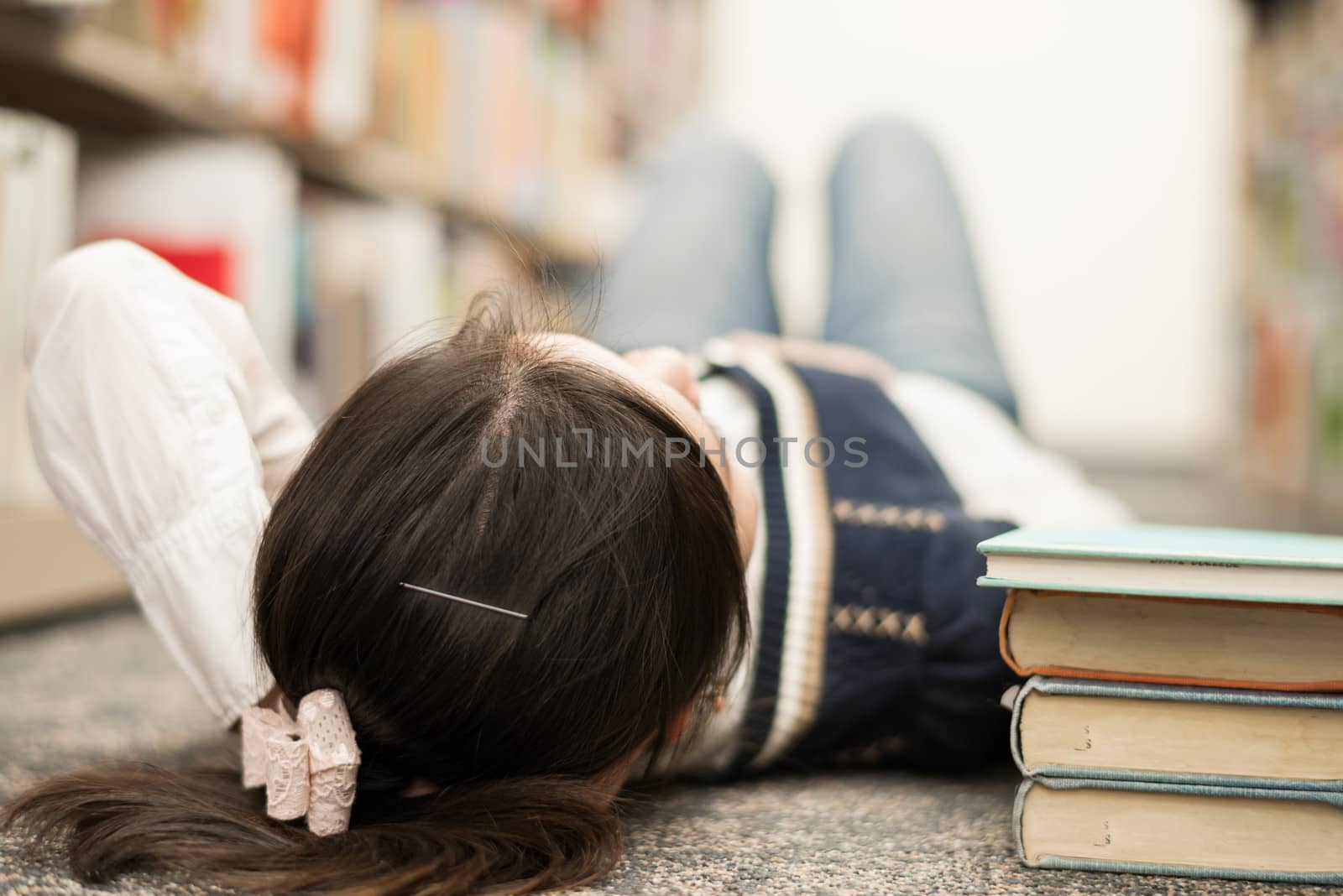 Young girl student laying on the library floor with a stack of books next to her