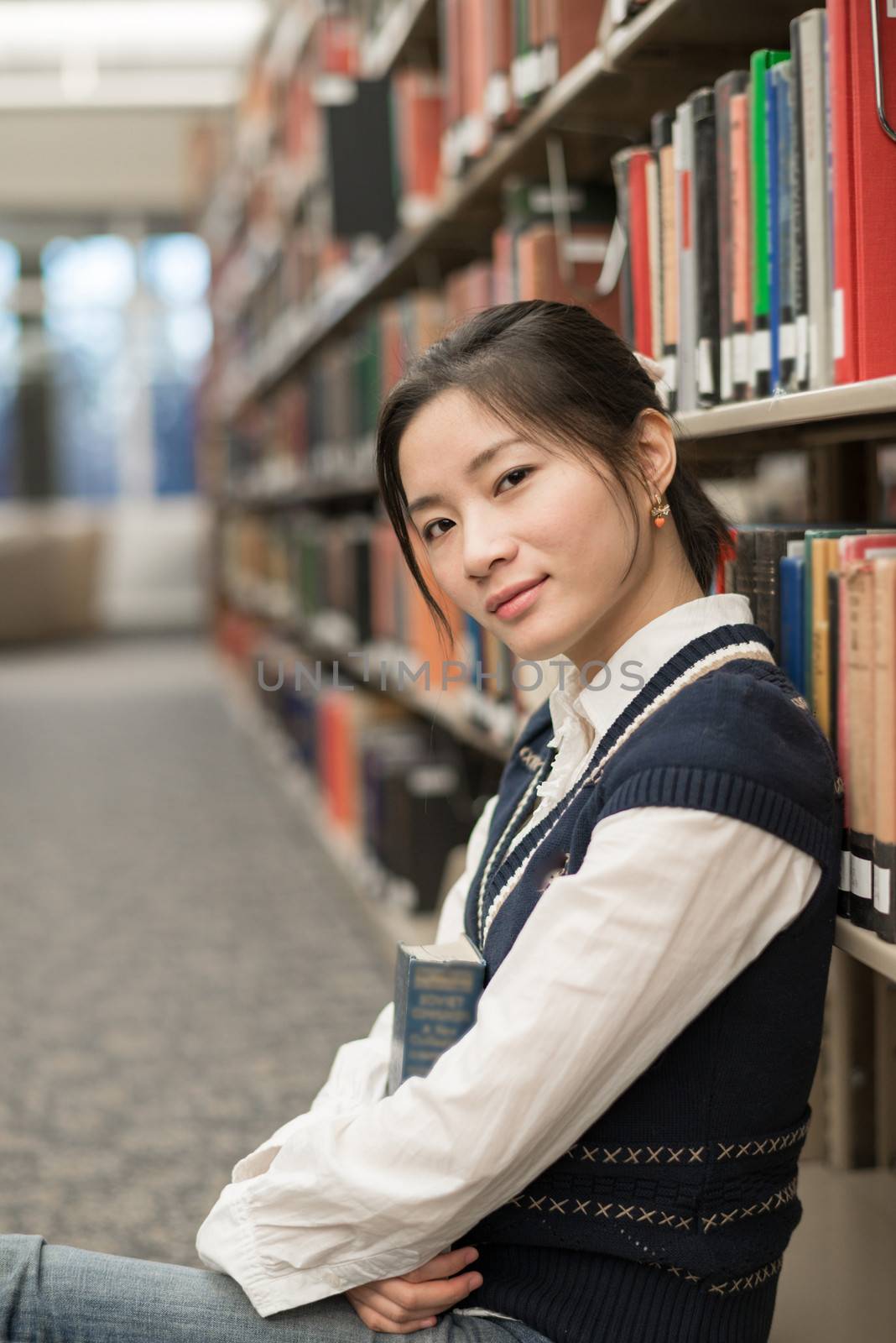 Portrait of attractive young girl sitting on the floor in front of a bookshelf holding a thick old book