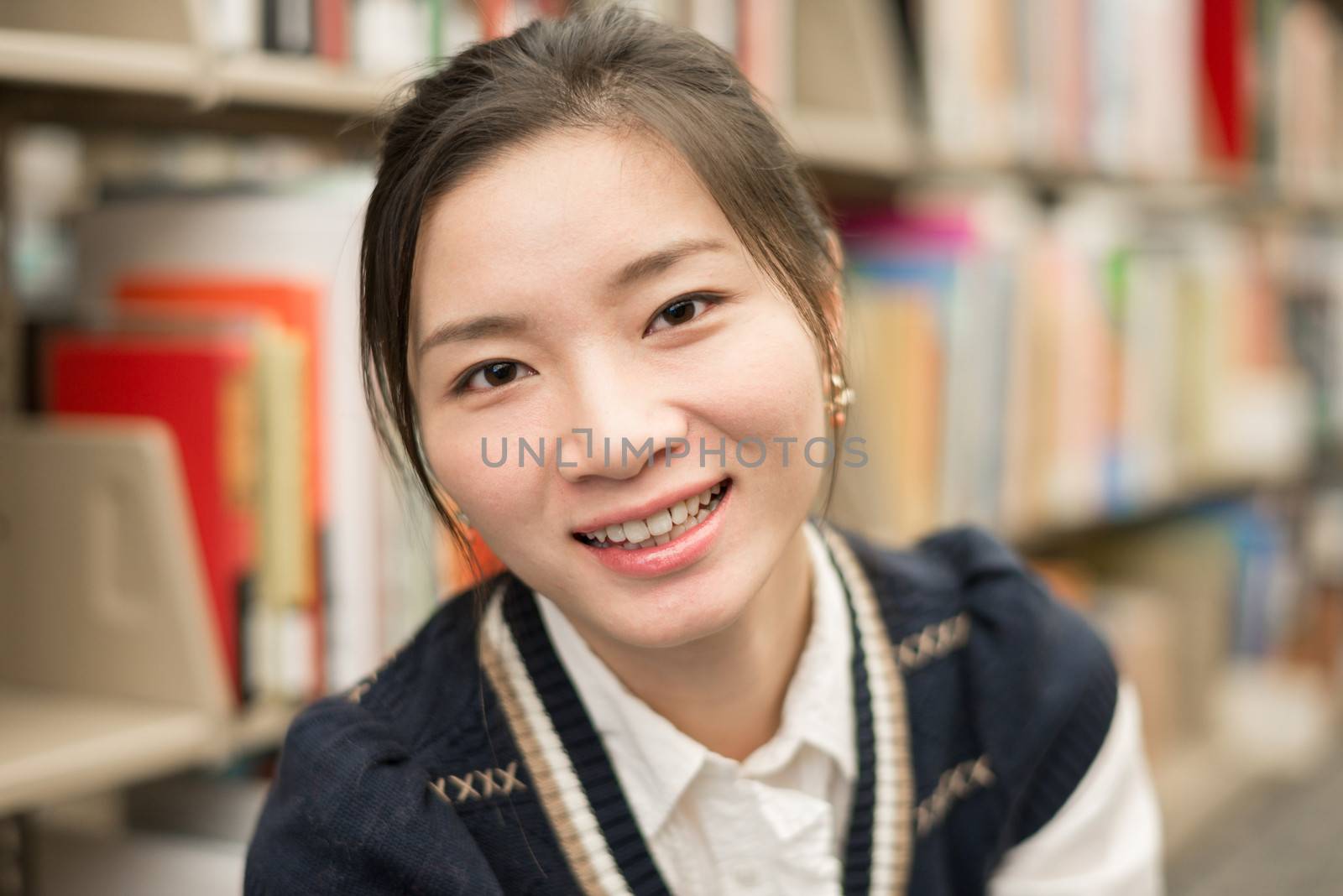 Portrait of attractive young girl smiling in library with bookshelf as background
