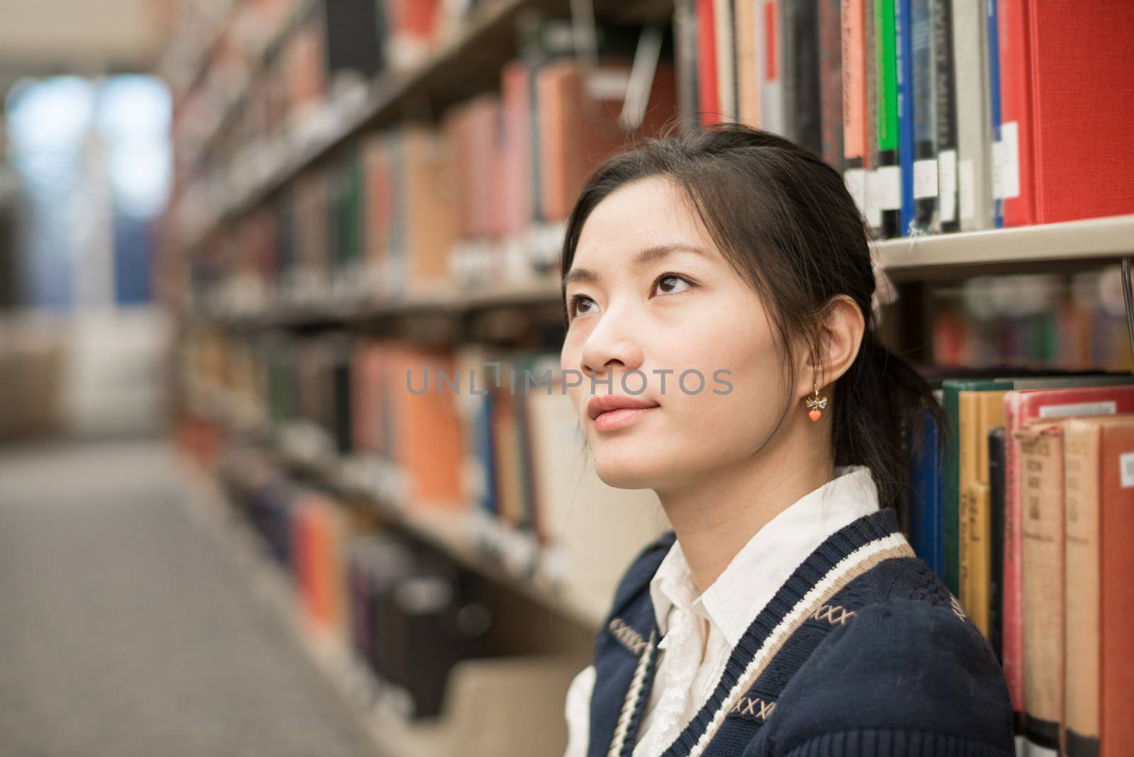 Emotional young woman sitting on the floor in next to a bookshelf in library