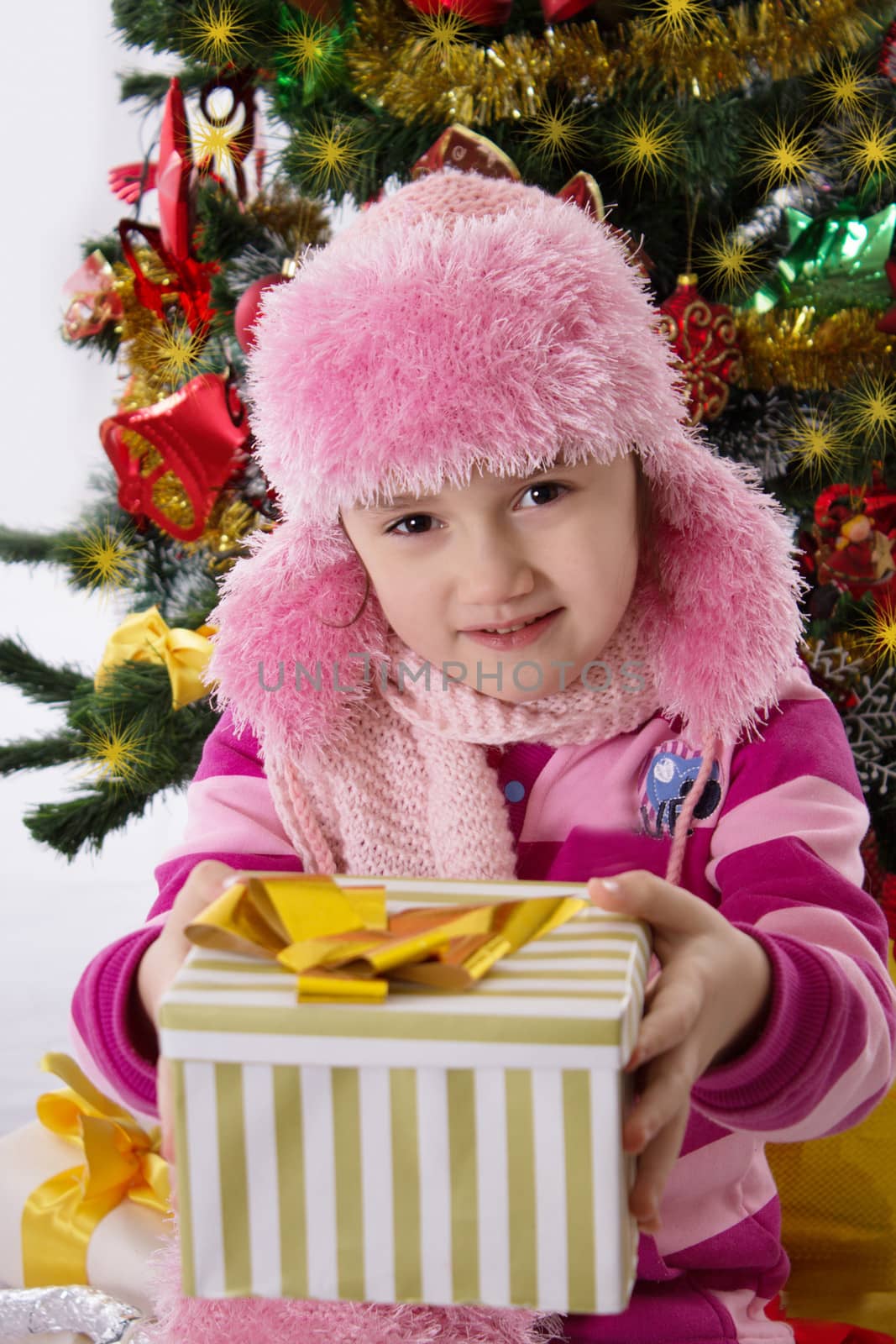 Pretty girl in pink fur hat holding present under Chritmas tree
