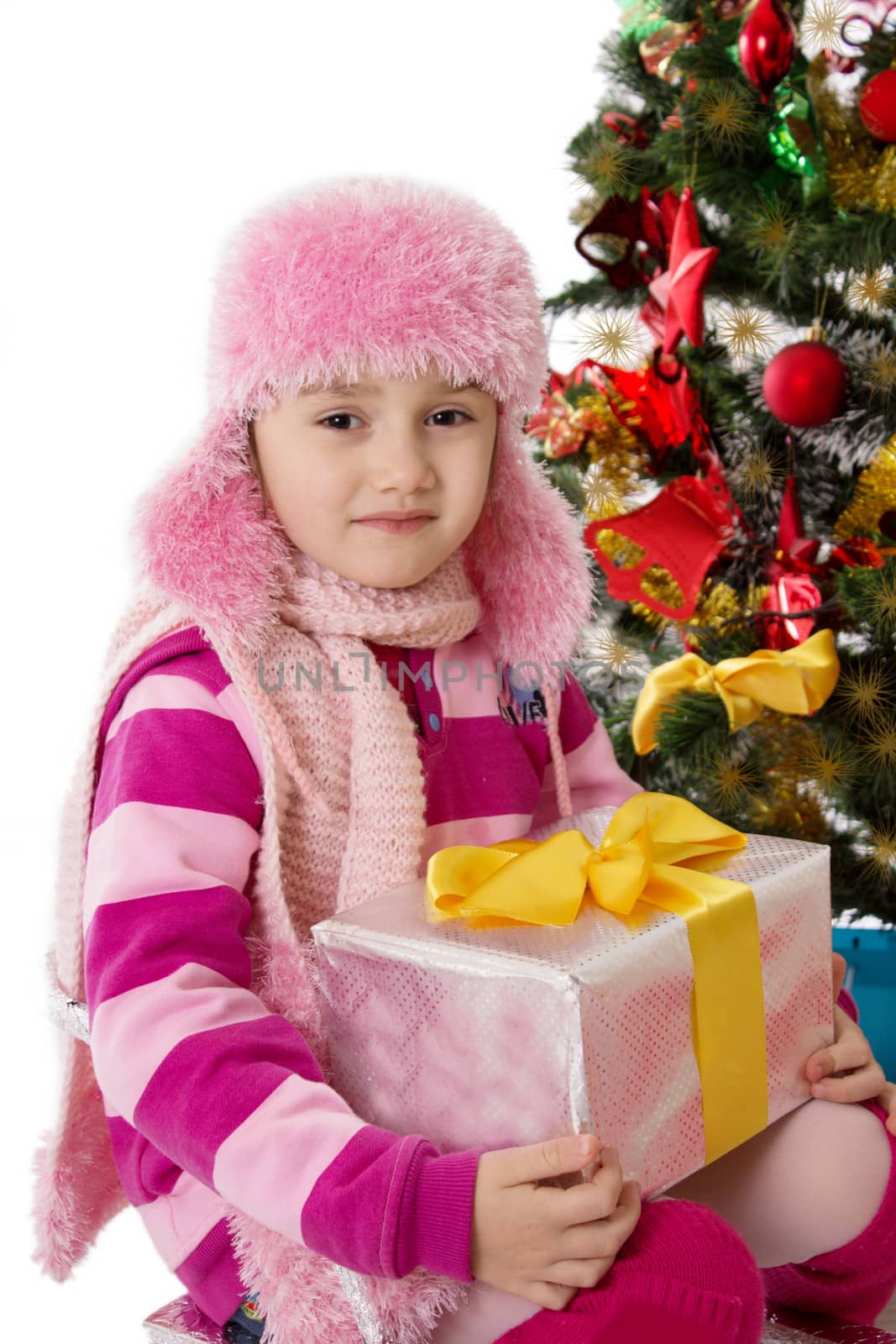 Girl in pink fur hat holding present under Chritmas tree by Angel_a