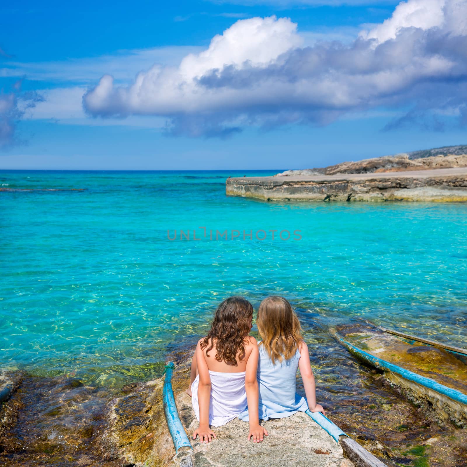 Blond and brunette kid sister girls sitting on beach port in Formentera summer vacation