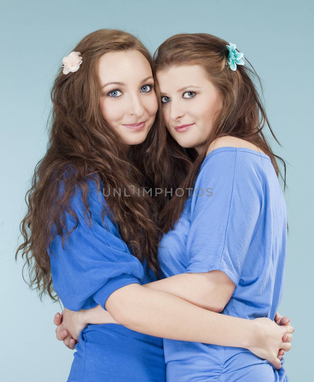 two young female friends hugging, looking - isolated on blue