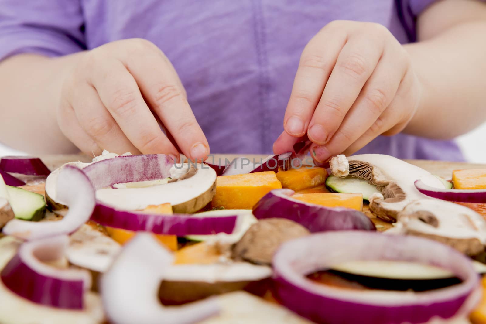 small hands preparing fresh pizza with many vegetables