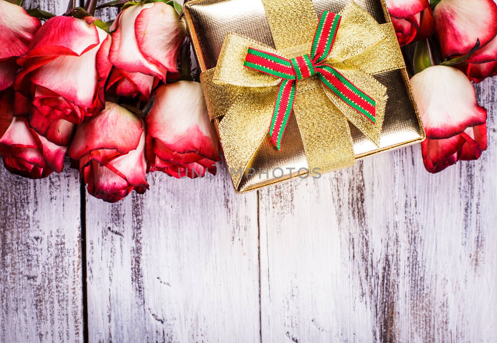 Golden gift box and bouquet of roses on white shappy painted wooden background