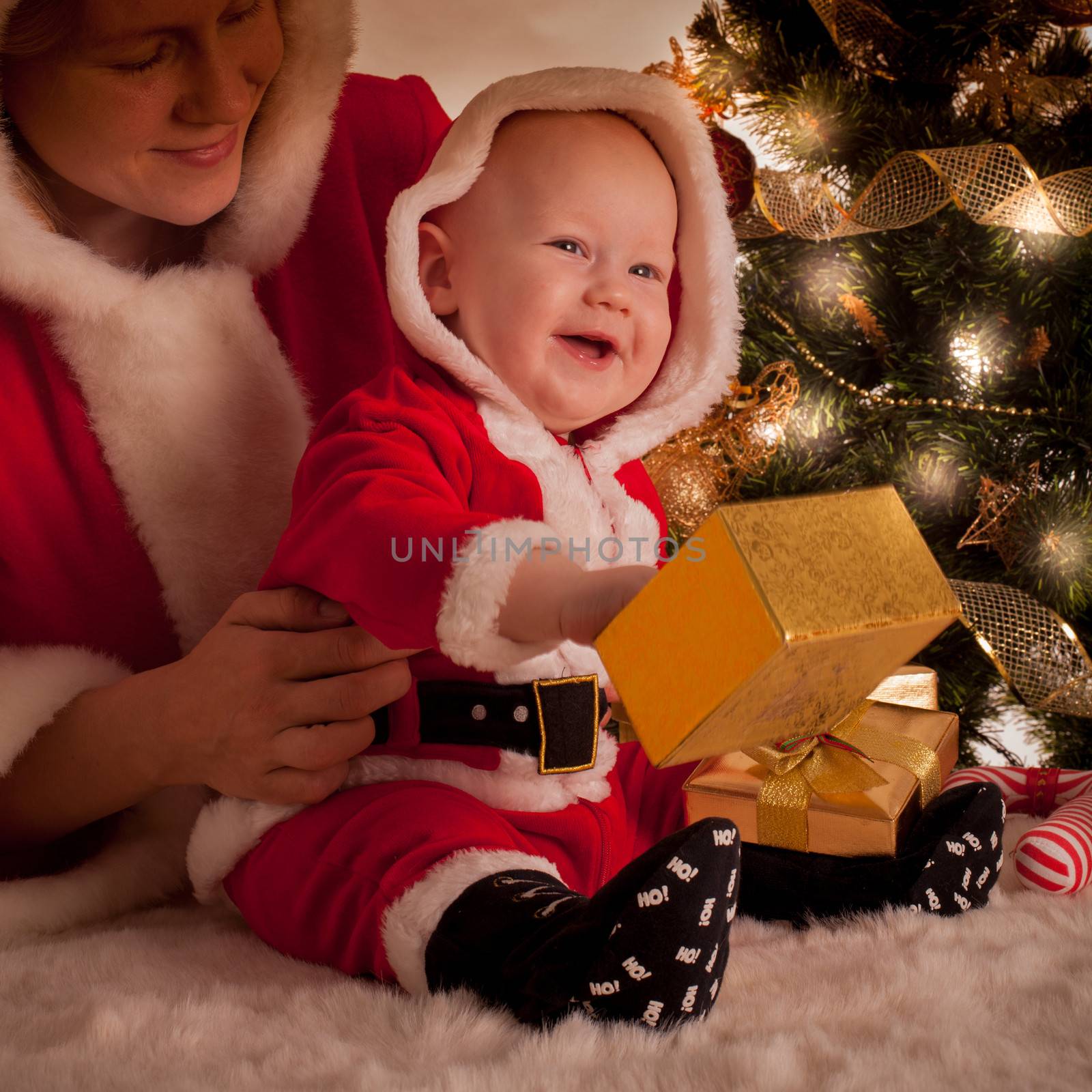 Christmas baby and mom open gifts under the fir tree
