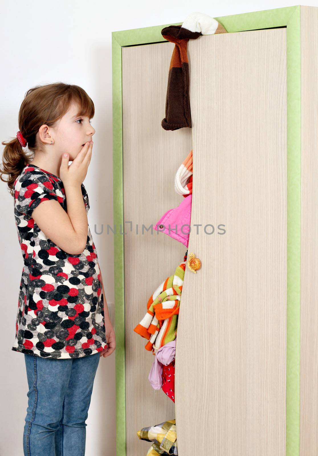 shocked little girl looking into a messy closet 