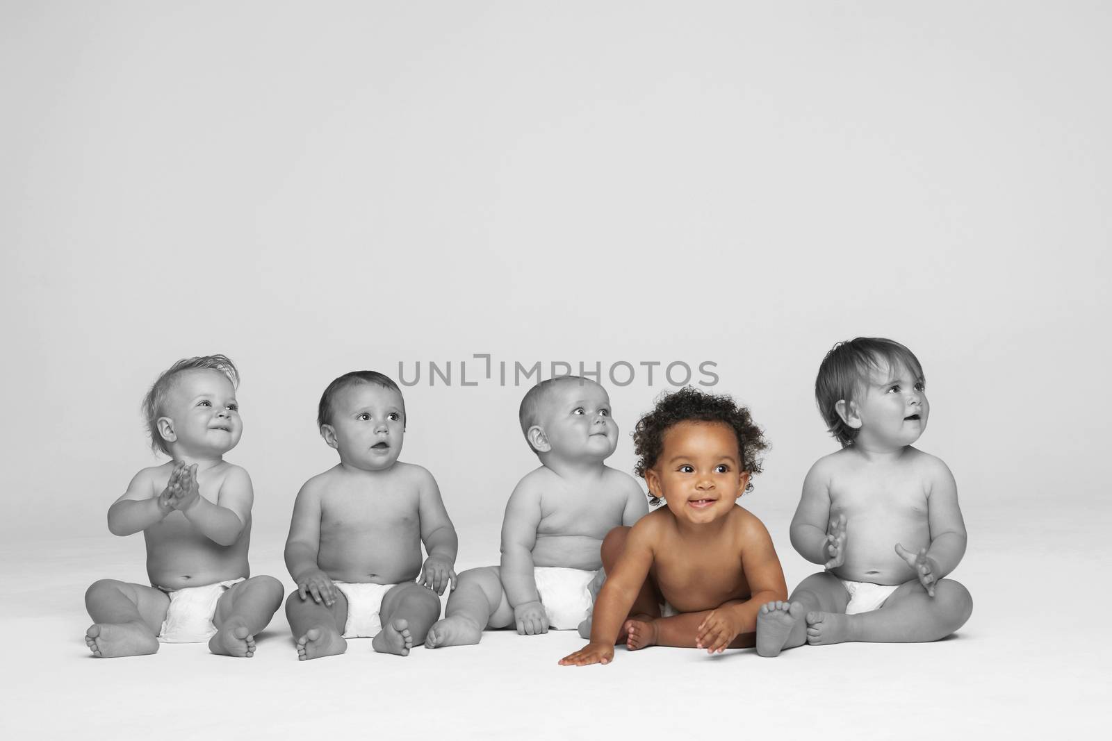 Baby girl sitting on floor with other babies looking away by moodboard
