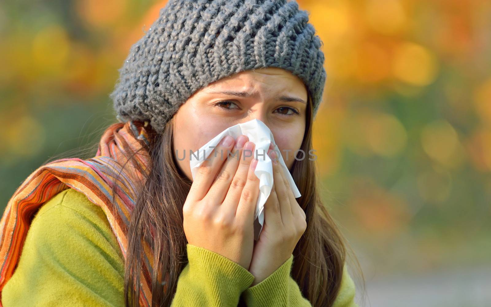 Sick young model isolated on autumn background blowing her nose