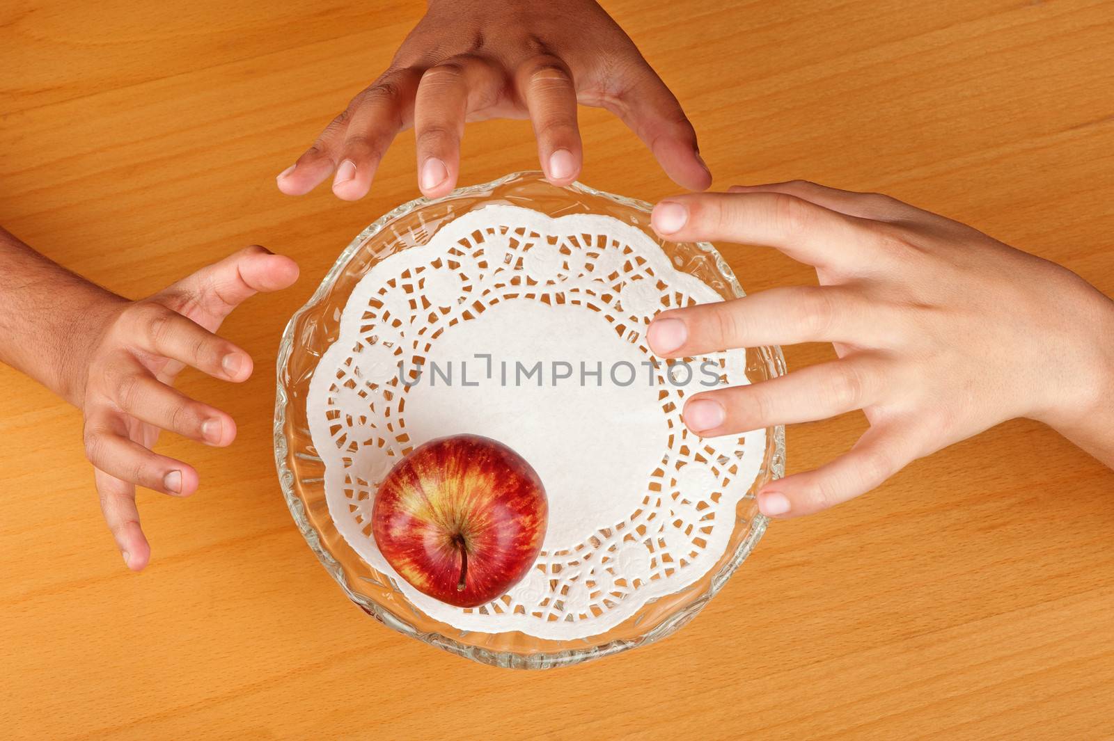 Children hands compete to grab the last apple available in a bowl.
