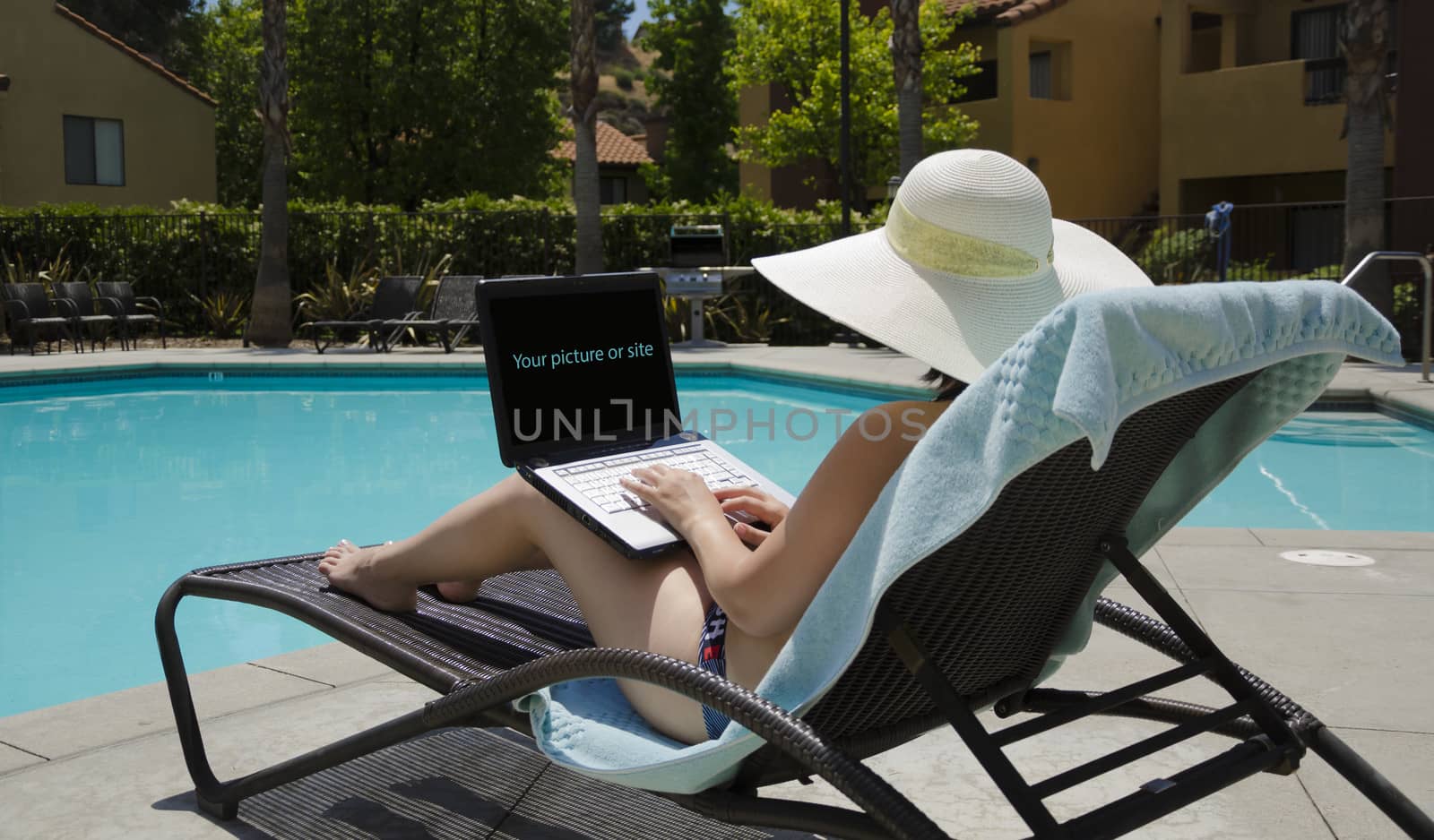 Girl in a summer heat typing on laptop by the swimming pool