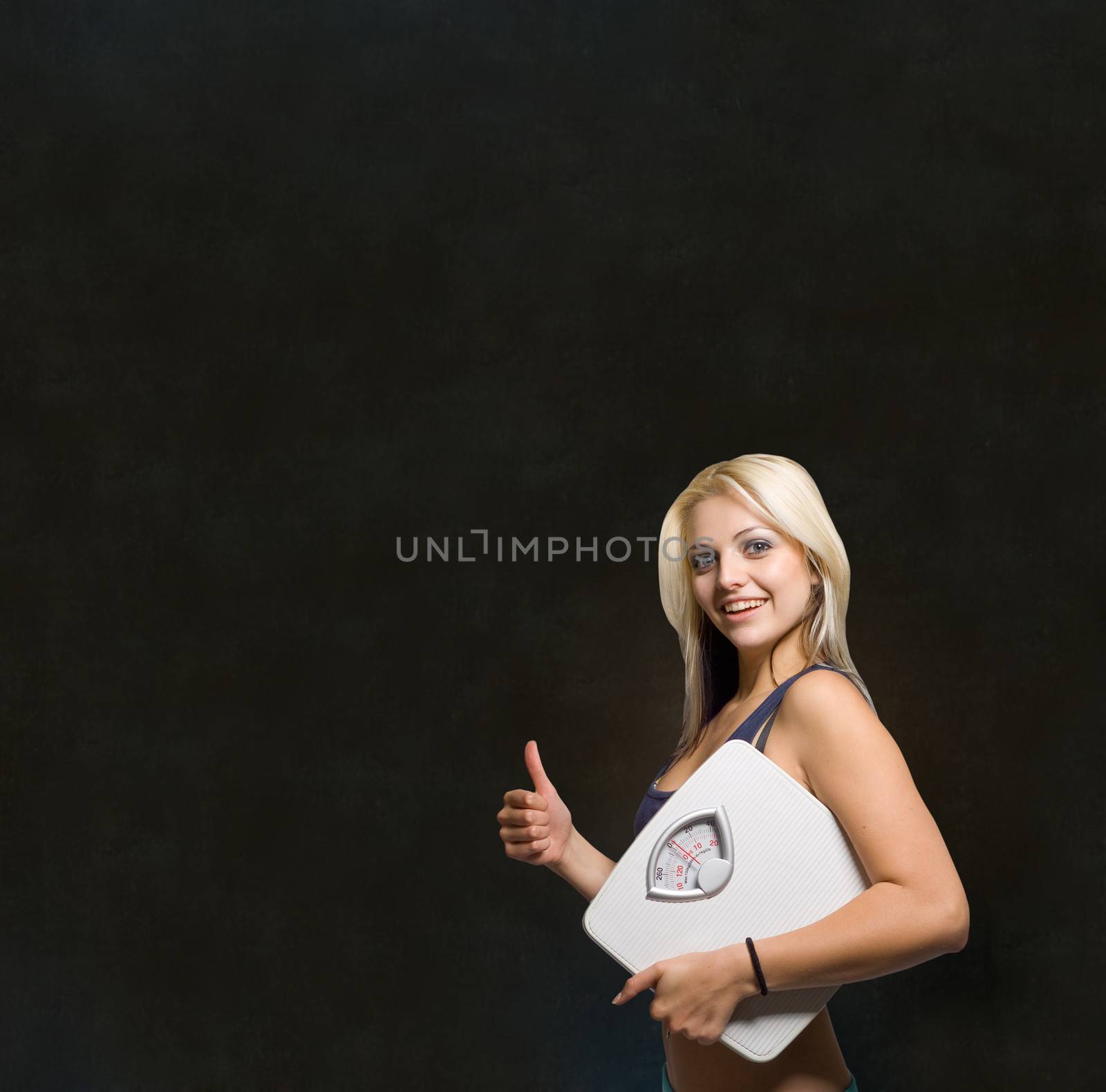 Beautiful young woman with weight scale on blackboard background