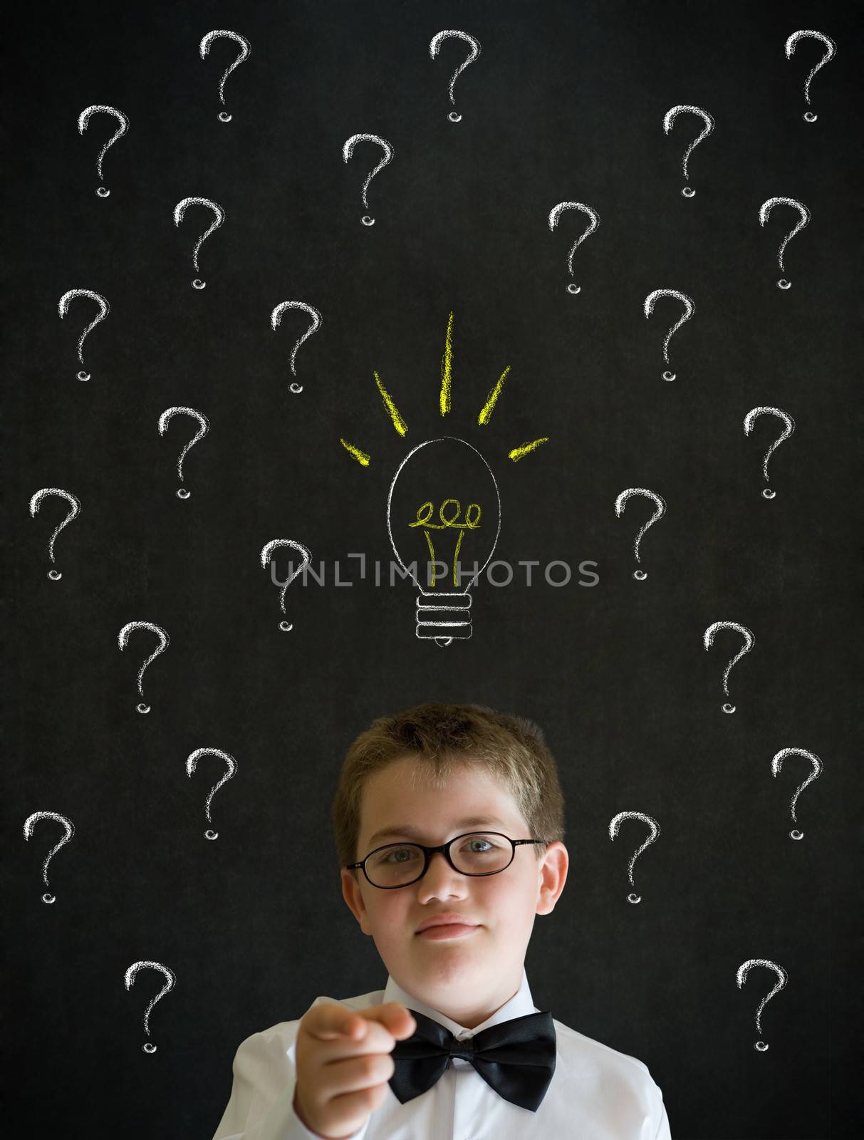 Pointing boy dressed up as business man questioning ideas on blackboard background